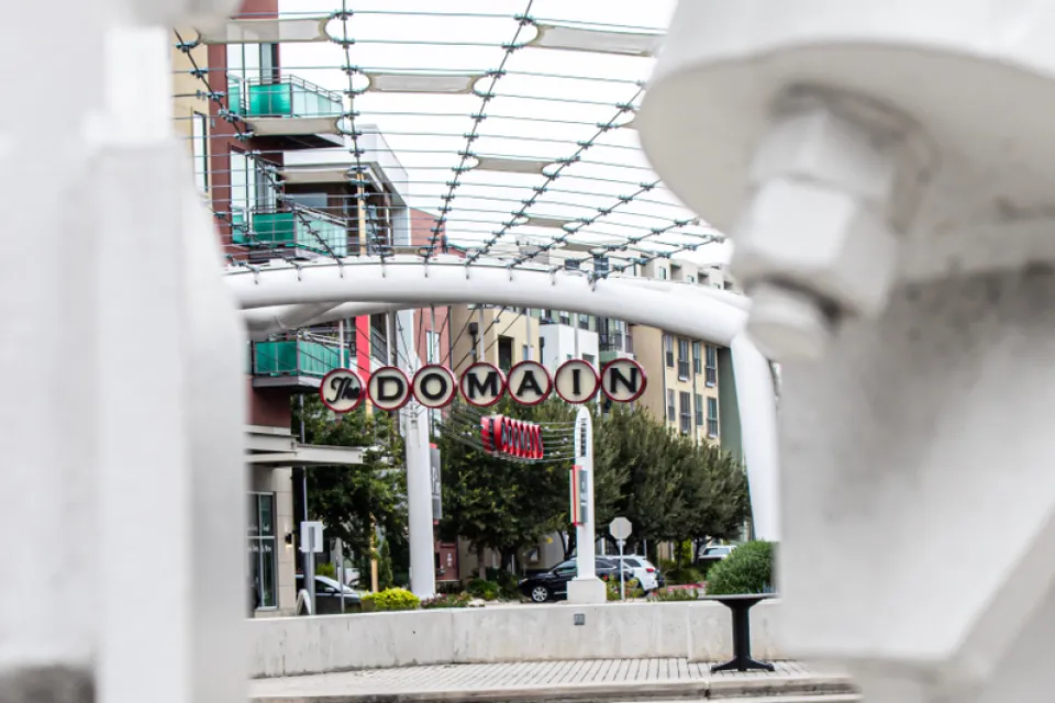 A picture of a decorative sign announcing “The Domain” surrounded by high density shops and apartments.